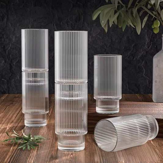 Set of clear glasses with ribbed design on a wooden surface with a dark textured wall background.