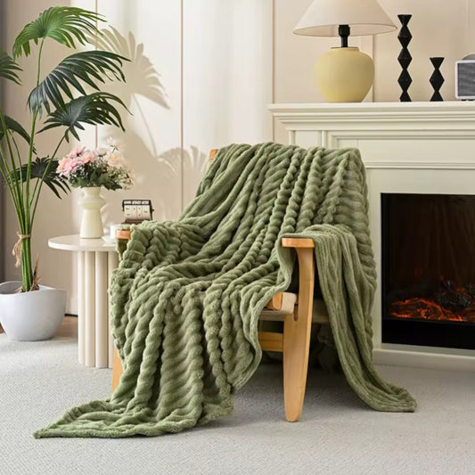 A deep green, chevron-textured soft throw blanket draped over a light wood armchair.