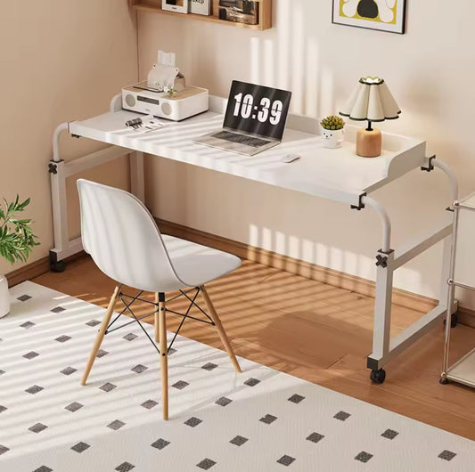 A white adjustable over bed desk with a white metal frame, set over a white rug on a wooden floor, holding a laptop and lamp, with a white chair pulled up to the side.