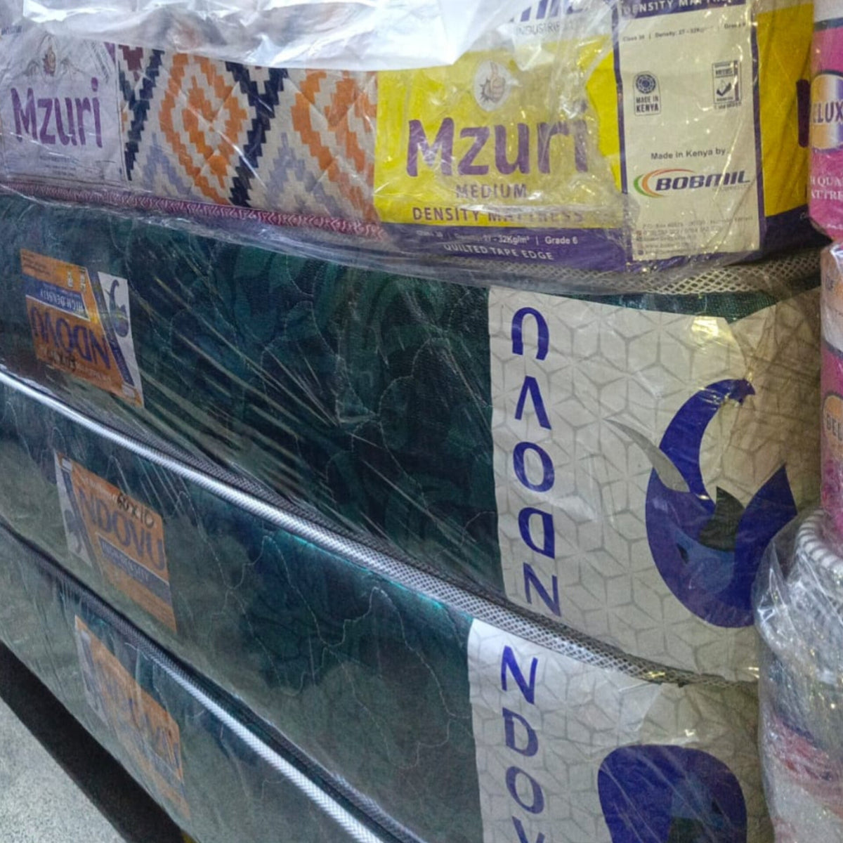 Stacked wrapped mattresses on display in store, including Mzuri and NDOON packaging