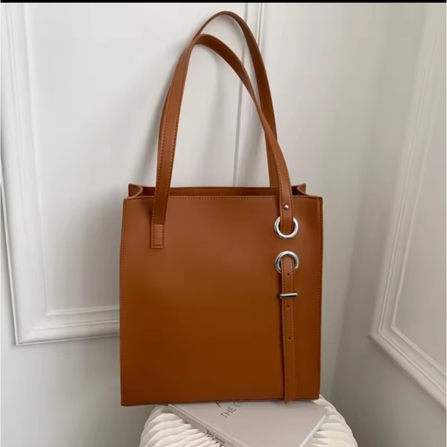 Brown structured vertical leather tote bag with long shoulder straps and decorative silver ring and buckle details.