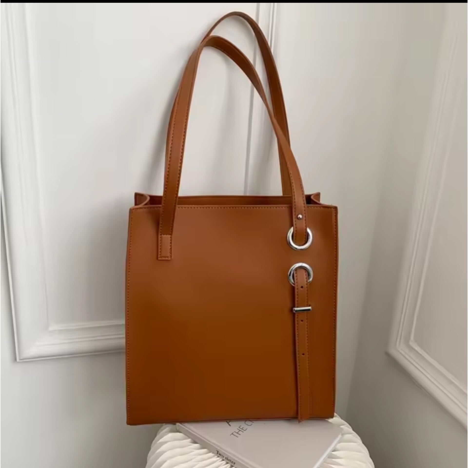 Brown structured vertical leather tote bag with long shoulder straps and decorative silver ring and buckle details.