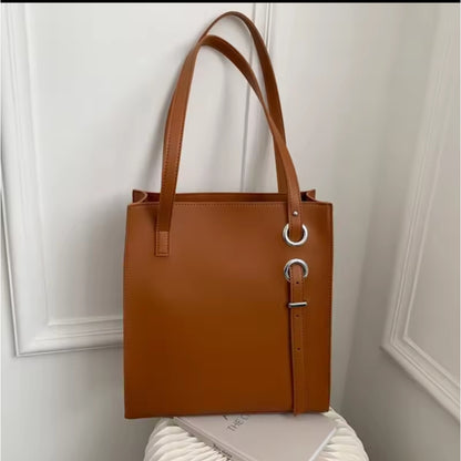 Brown structured vertical leather tote bag with long shoulder straps and decorative silver ring and buckle details.