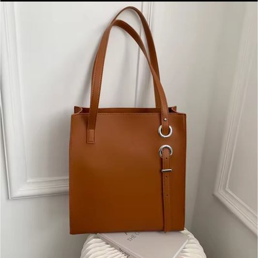 Brown structured vertical leather tote bag with long shoulder straps and decorative silver ring and buckle details.
