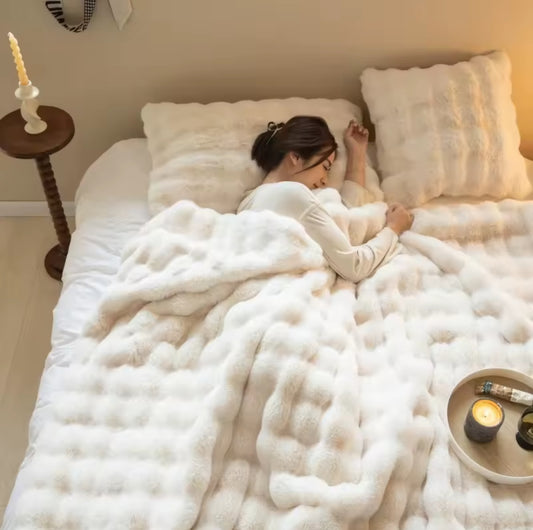 A woman sleeping comfortably in bed under a thick, creamy white throw blanket with a fluffy, square bubble texture.