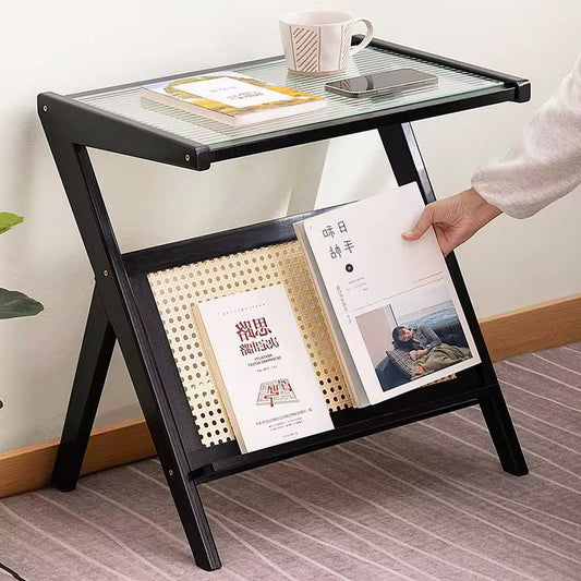 A dark brown wooden side table with a clear glass top and a woven rattan lower storage section.