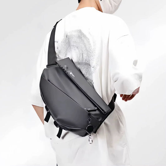 Man wearing a dark grey, minimalist ergonomic crossbody sling bag across his back and chest.
