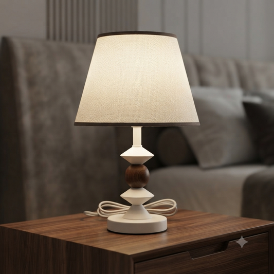 A table lamp with a warm white fabric drum shade, a white sculptural base, and a dark wood bead accent.