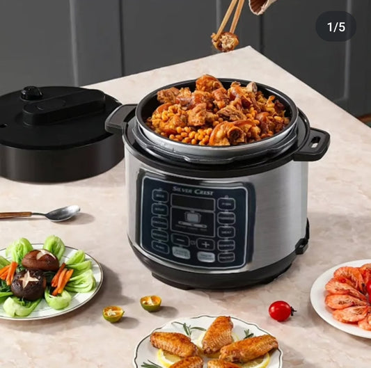 A silver and black electric pressure cooker with a digital screen, set on a counter with cooked meat and vegetables on plates around it.