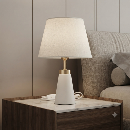 A modern table lamp with a white tapered base, a beige fabric drum shade, and a gold-finished neck.