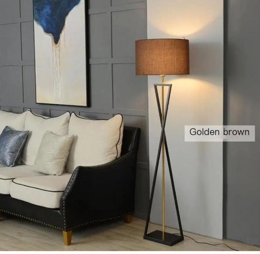 A floor lamp with a golden-brown fabric drum shade and a black and gold metal tripod base.