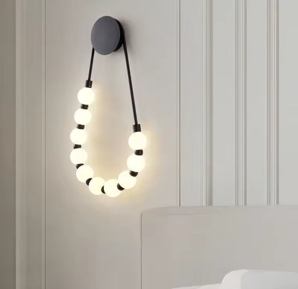 Wall lamp with a black circular mount holding a string of ten white globe light bulbs