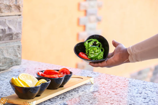 Three heart-shaped black ceramic bowls on a bamboo tray