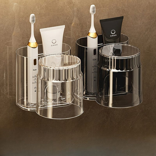 A wall mounted toothbrush rack featuring transparent and dark acrylic containers holding two electric toothbrushes and toothpaste tubes, with two ribbed rinsing cups inverted beneath the holders.