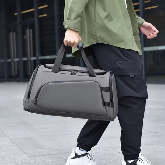 Person walking outdoors carrying a sleek, modern grey waterproof duffel bag with handles and subtle zippers.