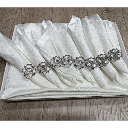 Boxed 17-piece table set with eight jacquard napkins and jeweled rings on a large matching tablecloth in a creamy white or ivory color.