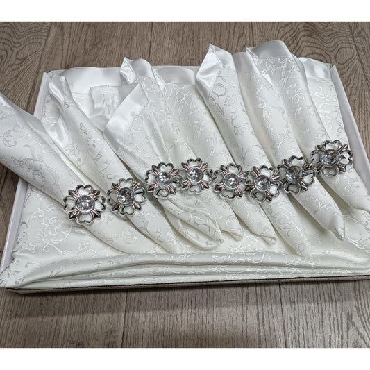 Boxed 17-piece table set with eight jacquard napkins and jeweled rings on a large matching tablecloth in a creamy white or ivory color.