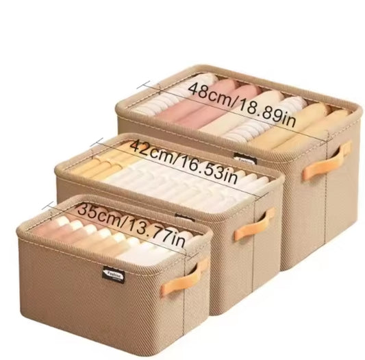 Three rectangular beige fabric storage boxes of increasing size, with clothes neatly folded inside, showing dimensions in centimeters and inches.