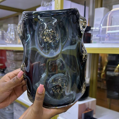 A hand holding a heavy-duty smoky glass vase with gold-infused abstract patterns.