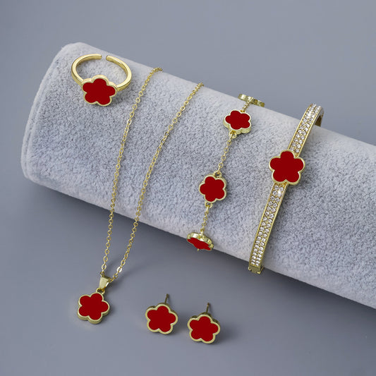 A jewelry set with red flower shaped details, including a necklace, ring, earrings, chain bracelet, and crystal studded bangle, displayed on a gray surface.