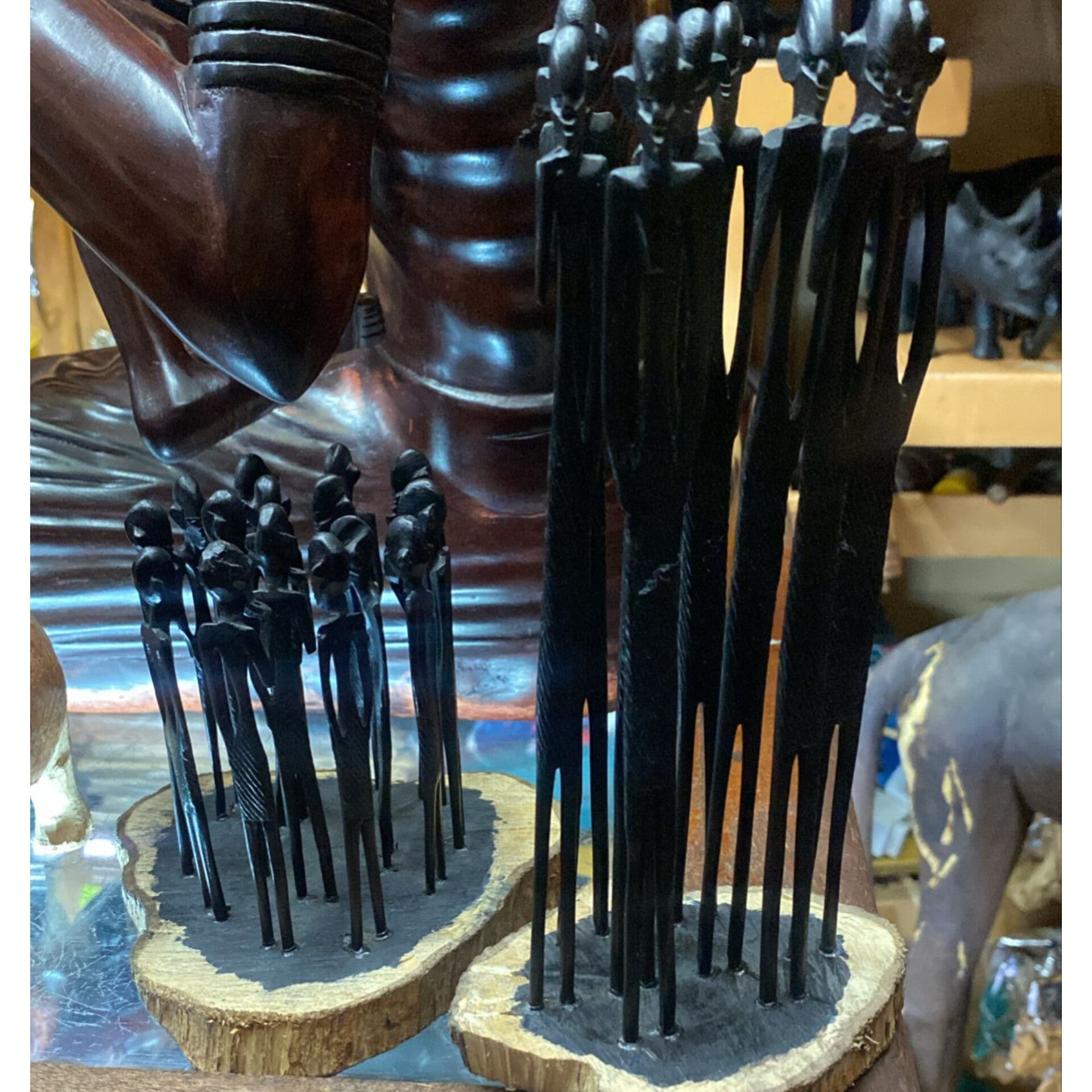 A group of slender, dark hand-carved Wooden stick figures standing upright on natural wood bases.