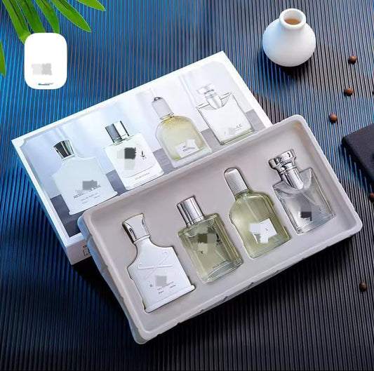 A gift box containing four miniature glass bottles of men's cologne, two in white bottles and two in clear glass, displayed on a dark surface.