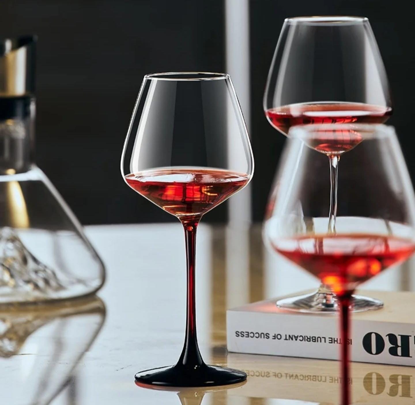 Six elegant crystal wine glasses with clear bowls, red stems, and black bases