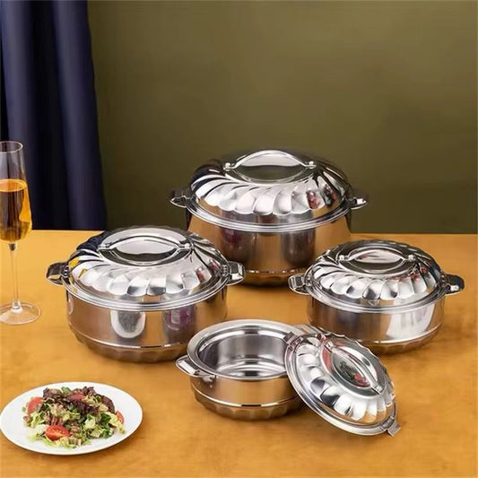 A set of four shiny, stainless steel insulated hotpots with scalloped designs, arranged on a yellow table with a plated meal and a wine glass nearby.
