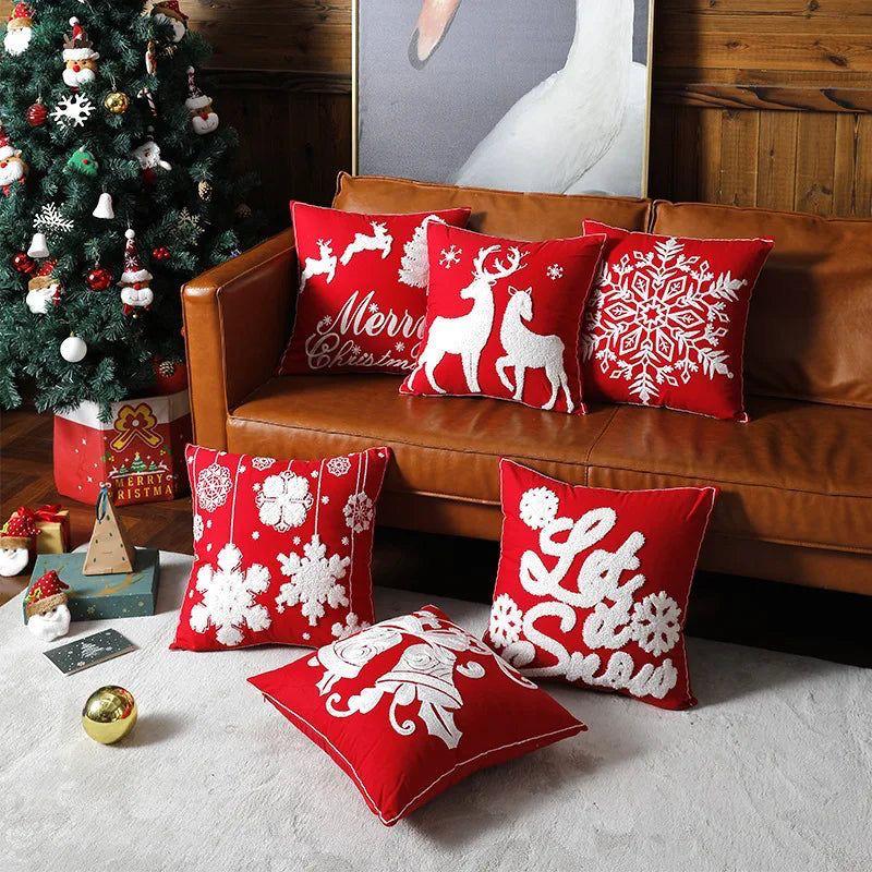 Six red Christmas pillow covers with white embroidery featuring snowflakes, reindeer, a bell, and holiday phrases