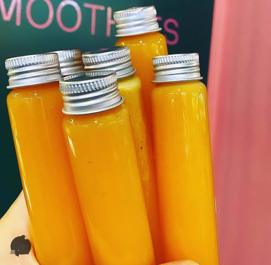 A group of six ginger shot bottles with metal caps, displayed upright.
