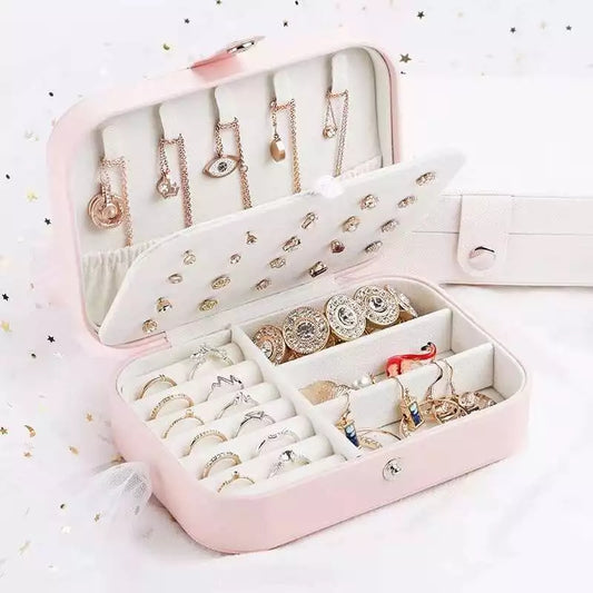 An open pink travel jewelry box displaying necklaces, earrings, and rings in organized slots.