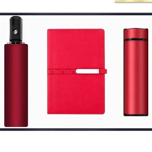 A professional gift set containing three items: a red smart vacuum flask, a red notebook or diary, and a compact black and red umbrella